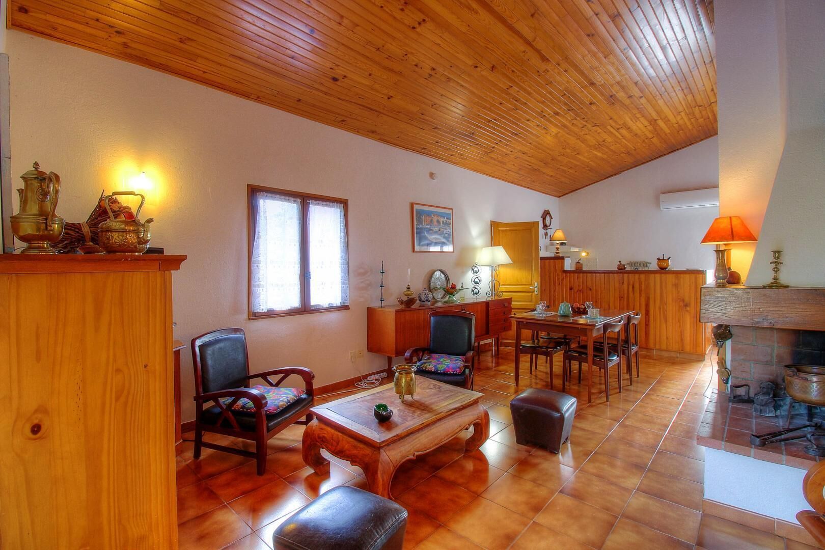 A spacious living room with wooden flooring, a fireplace, a dining area, and a kitchen in the background.