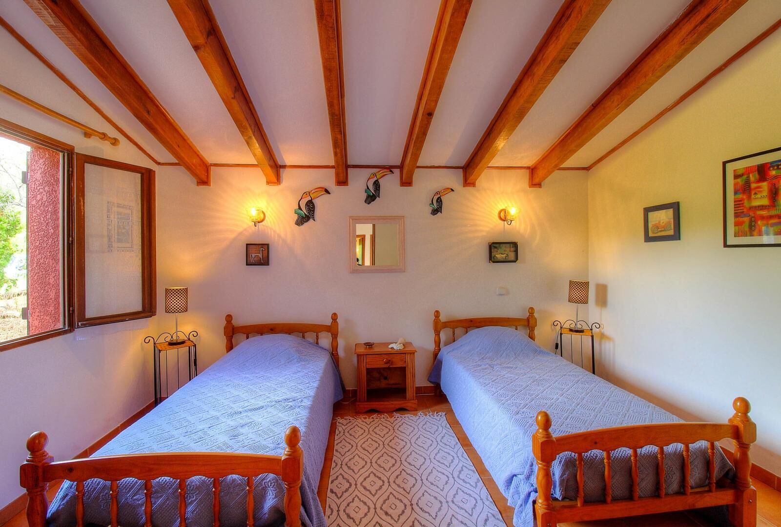 A room with two wooden beds, a small table, a mirror, and wall-mounted lights.