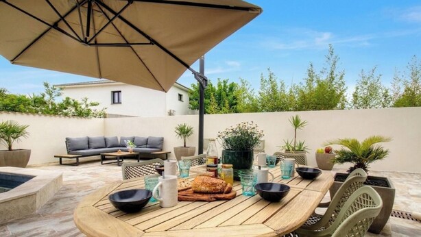 Un espace extérieur aménagé pour les repas, avec une table ronde, des chaises, un canapé et un parasol.