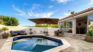 Une piscine avec un parasol, des sièges d’extérieur et un espace patio.