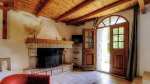 Una habitación con chimenea, vigas de madera, revestimiento de piedra para la chimenea y una puerta que da al exterior.