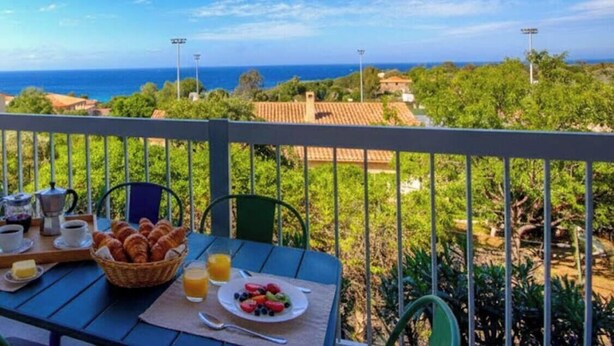 A balcony with a table set for breakfast, overlooking a coastal landscape with houses and trees. - Casa Mea - MONTICELLO (MONTICELLO)