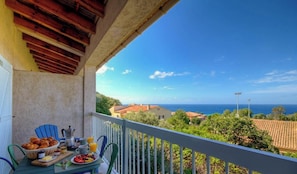 A balcony with a table set for breakfast, overlooking a coastal view with houses and the sea. - Casa Mea - MONTICELLO (MONTICELLO)