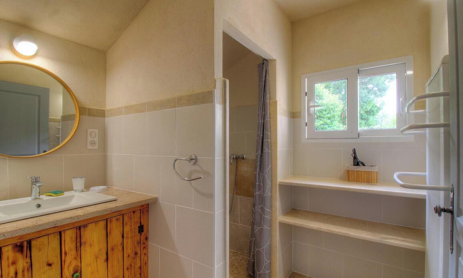 Un bagno con un mobile vanitario in legno, uno specchio, una doccia e una finestra.
