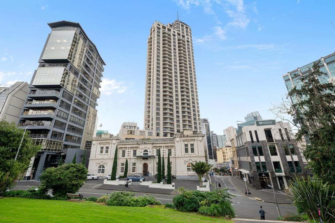 Een hoog, modern gebouw met een centrale ingang en een omliggend groen gebied.