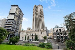 A tall, modern building with a central entrance and a surrounding green space. - Cute with a View & Carparking too (Auckland CBD)