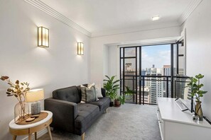 A modern living room with a sofa, a side table, a lamp, and a view of the city through large windows. - Cute with a View & Carparking too (Auckland CBD)