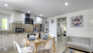 A modern kitchen with a dining area, a sofa, and a clock on the wall. - A Foce - ALTAGENE - Gîte (ALTAGENE)
