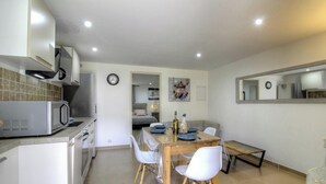 Cocina compacta equipada con microondas, estufa y lavaplatos. Se encuentra una mesa de comedor con sillas y un refrigerador pequeño.