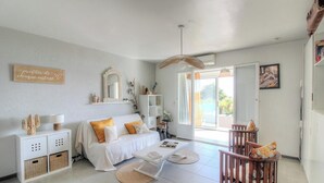 A room with a bed, a white sofa, a wooden chair, a small table, a bookshelf, a mirror, and a sliding glass door leading to an outdoor area. - AICCU BELLU - AJACCIO (AJACCIO)