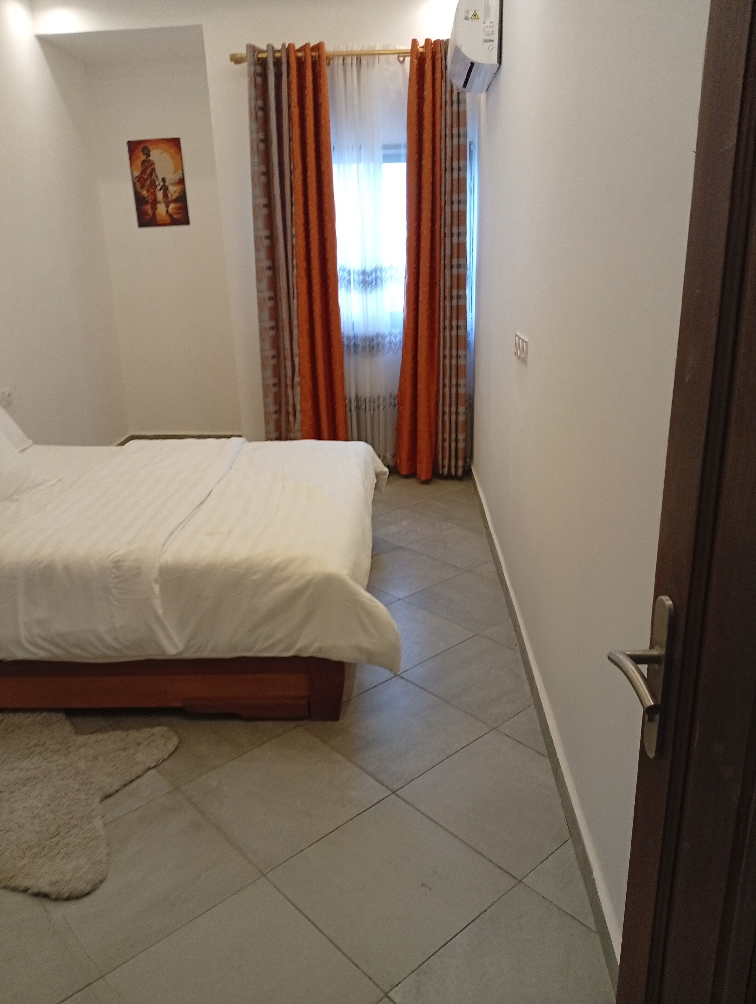 Een slaapkamer met een bed, gordijnen, een wandairconditioner en een klein vloerkleed.