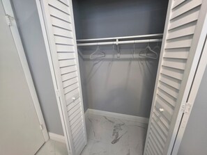 Un dressing avec des portes Ă persiennes blanches, une tringle Ă vĂȘtements et un revĂȘtement de sol imitant le marbre.