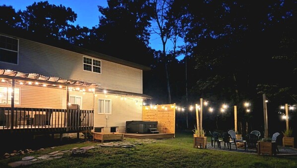 A house with a deck, outdoor seating, and string lights. - Poconos Group Getaway: Hot Tub, Fire Pit & Pet Friendly (Lakeville)