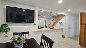 Un comedor con televisión, sillas de madera, una mesa y una planta en maceta.
