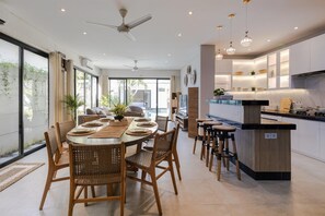 A modern kitchen with a central island, dining area with wicker chairs, and a ceiling fan. - Villa Ariki - Stylish Sanur Escape (Denpasar)