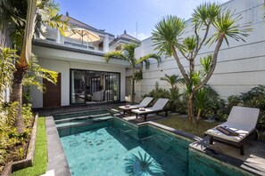 A pool area with lounge chairs, a glass-enclosed room, and tropical plants. - Villa Ariki - Stylish Sanur Escape (Denpasar)