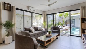 Ein modernes Wohnzimmer mit einer Couch, Sesseln, einem Couchtisch und Blick auf einen Swimmingpool.