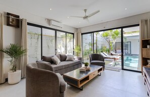Ein modernes Wohnzimmer mit einer Couch, Sesseln, einem Couchtisch und Blick auf einen Swimmingpool.