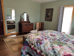 Une chambre à coucher avec un lit, une commode, un miroir et une vue sur une autre chambre à coucher, visible à travers une porte.
