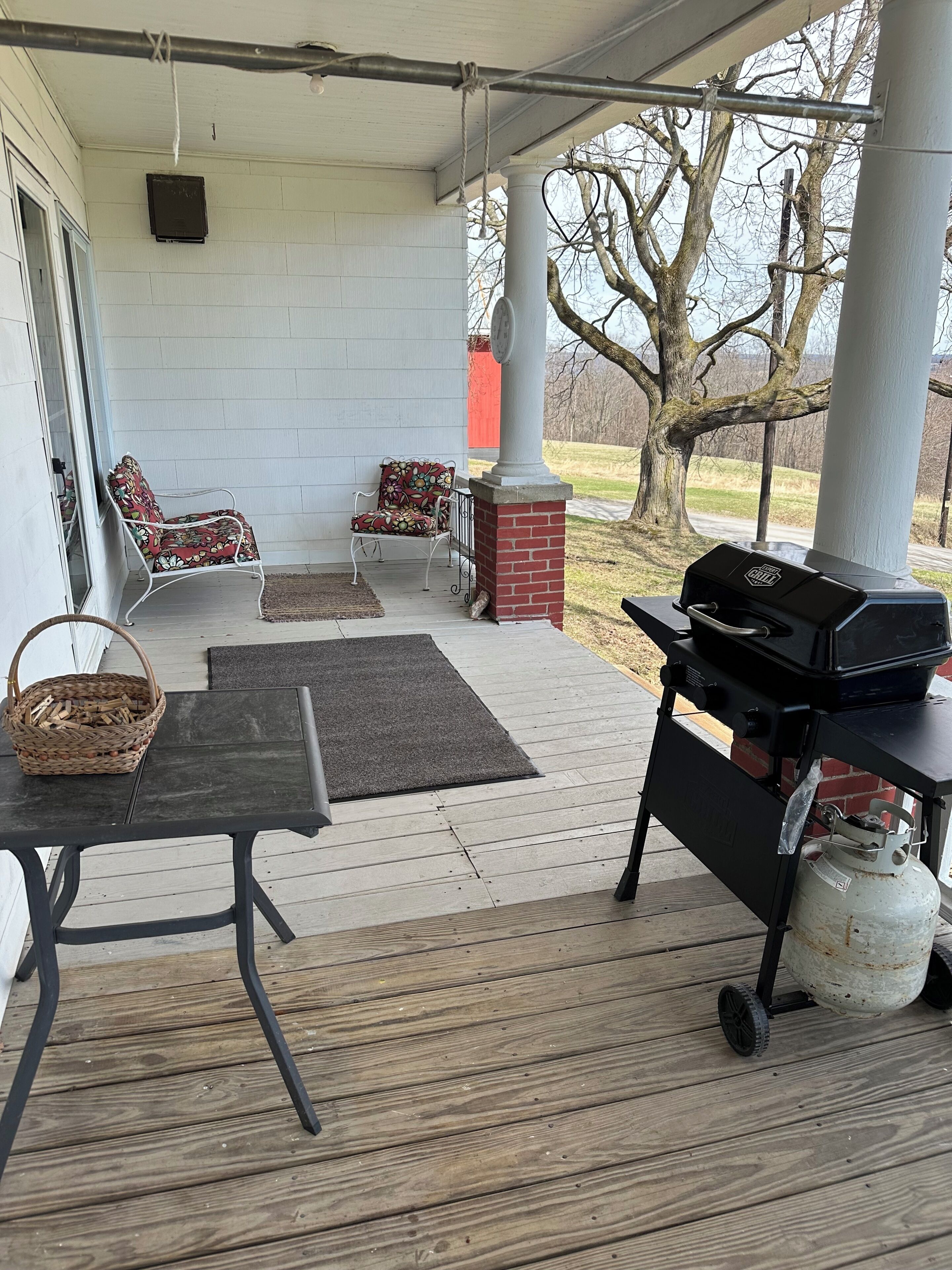A covered porch with a grill, two chairs, a table, and a basket.