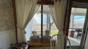 A room with a window, a chair, a table with a quilt, and a clock. - Peaceful country farmhouse, 2 bedrooms-all amenities for your comfort ! (Dansville)
