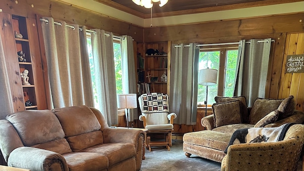 A cozy living room with a brown leather sofa, a patterned armchair, and a wooden bookshelf. - Peaceful country farmhouse, 2 bedrooms-all amenities for your comfort ! (Dansville)
