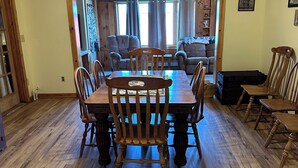 A dining area with a wooden table and chairs, a ceiling fan, and a view into a living room with a couch and curtains. - Peaceful country farmhouse, 2 bedrooms-all amenities for your comfort ! (Dansville)