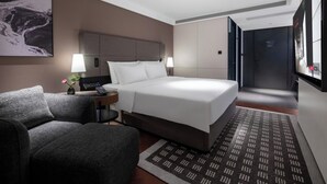 Quarto de hotel com cama, escrivaninha, cadeira, abajur e uma janela grande.