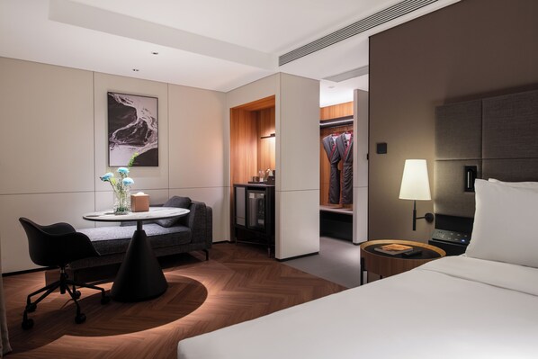 Habitación de hotel con cama, escritorio y silla, una mesita con un florero, perchero y armario.