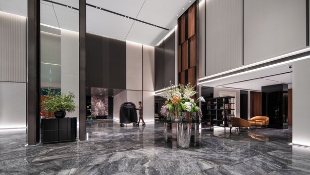 Um lobby moderno com piso de mármore, um arranjo floral central e uma área de estar com sofá e poltronas.