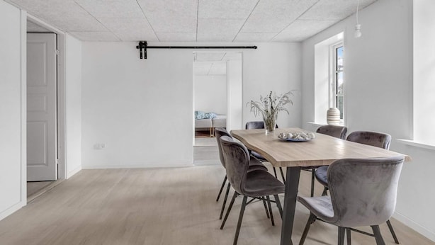 A modern dining area with a wooden table, grey upholstered chairs, and a hanging light fixture. - 4 Star Holiday Home in Spottrup (Spøttrup)