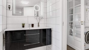 A modern bathroom with white tiled walls, a black vanity, a mirror, and a glass door leading to a laundry area. - 4 Star Holiday Home in Spottrup (Spøttrup)