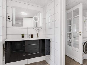A modern bathroom with white tiled walls, a black vanity, a mirror, and a glass door leading to a laundry area. - 4 Star Holiday Home in Spottrup (Spøttrup)
