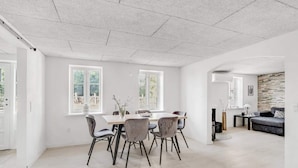 A spacious room with a dining table and chairs, large windows, and a stone accent wall. - 4 Star Holiday Home in Spottrup (Spøttrup)