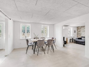 A spacious room with a dining table and chairs, large windows, and a stone accent wall. - 4 Star Holiday Home in Spottrup (Spøttrup)
