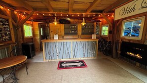Un interior rústico con techo de madera, una zona de bar con estantes, una chimenea y una mesa de comedor.