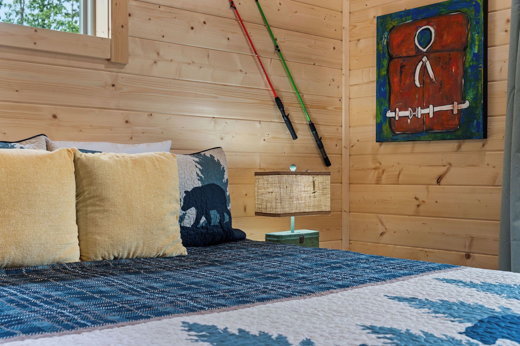 A wooden room with a bed, pillows, a lamp, and a painting on the wall.