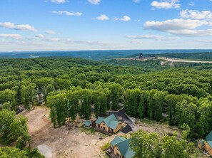 Uma área arborizada com um pequeno conjunto de construções, incluindo uma pousada com telhado verde, cercada por árvores densas.