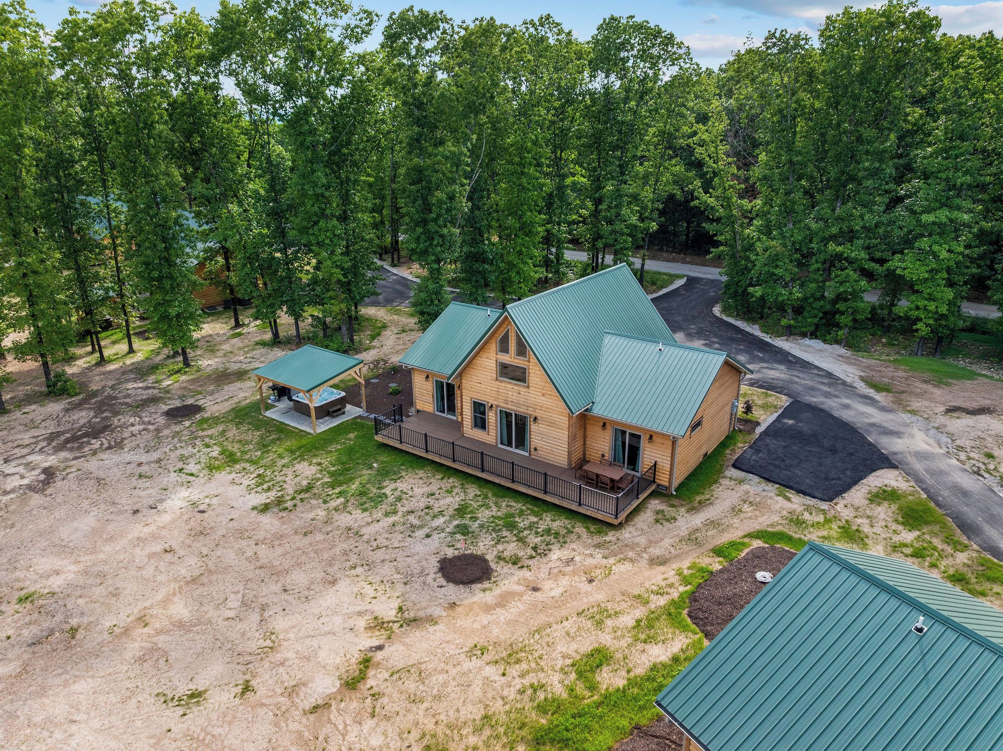A two-story log cabin with a green metal roof, surrounded by a wooded area.