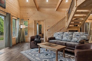 A wooden interior with a sofa, armchairs, a coffee table, and a staircase. - Authentic Log Cabin w Private Hot Tub_Near Big Cedar & Thunder Ridge_Free Tickets_Bonus Loft (Ridgedale)