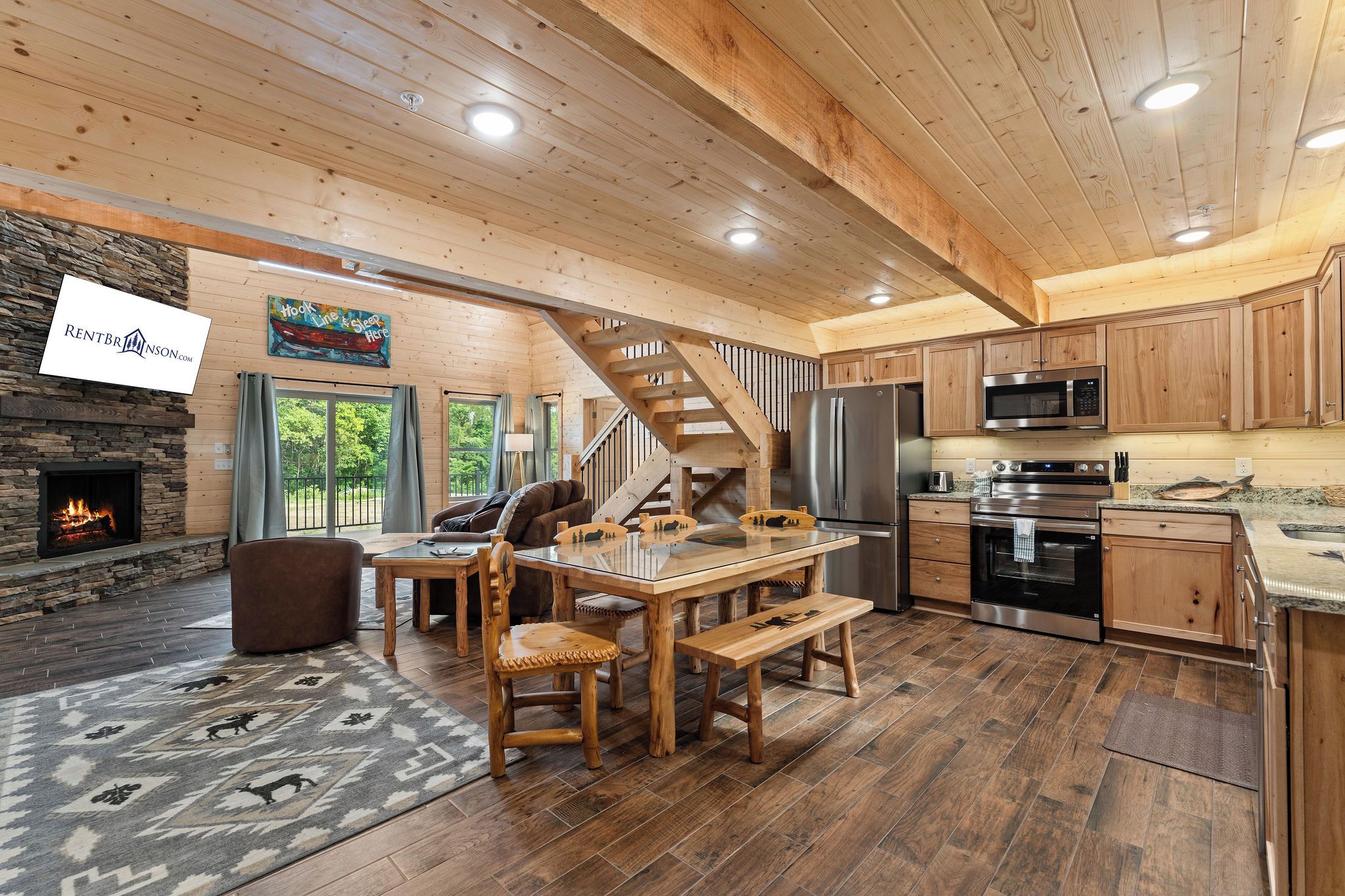 A spacious living area with a stone fireplace, wooden ceiling, and a dining table with chairs.