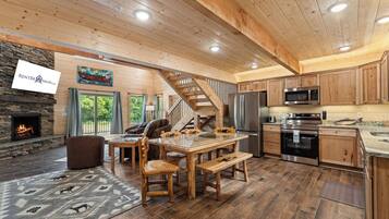 A spacious living area with a stone fireplace, wooden ceiling, and a dining table with chairs.