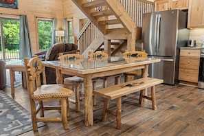 A wooden interior with a glass-top dining table, chairs, a bench, a kitchen area with a refrigerator, and a staircase. - Authentic Log Cabin w Private Hot Tub_Near Big Cedar & Thunder Ridge_Free Tickets_Bonus Loft (Ridgedale)