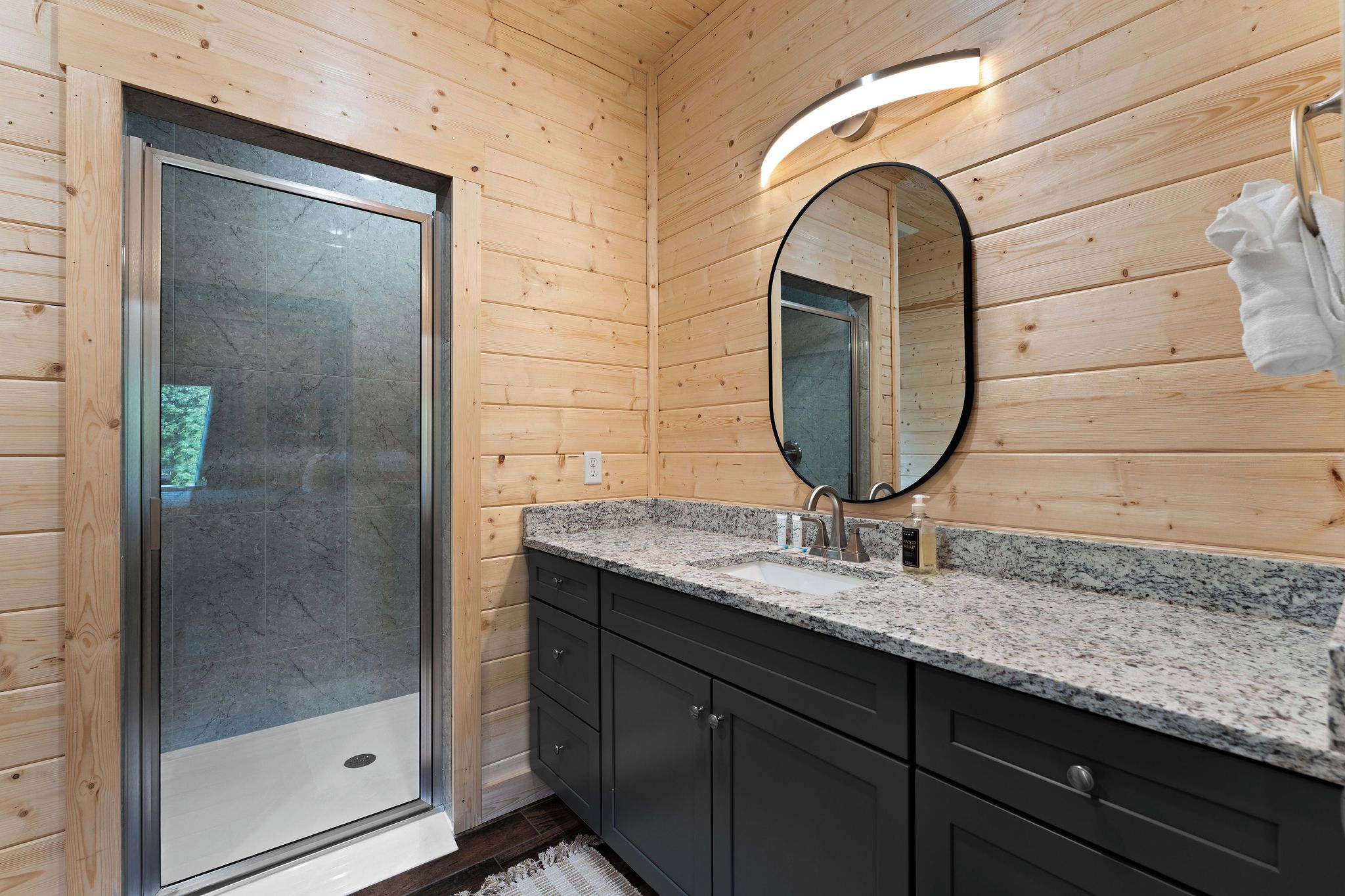 A modern bathroom with a shower, a sink with a mirror, and wooden walls.