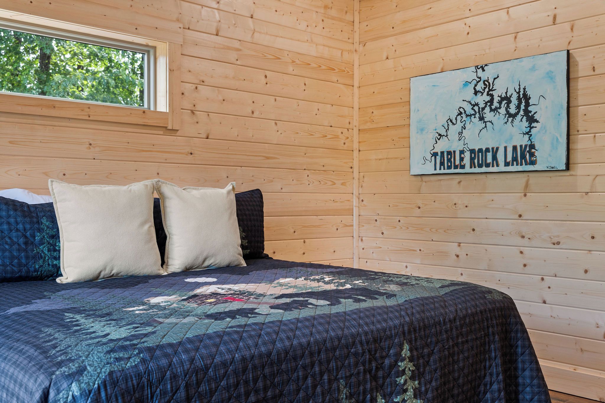 Habitación de cabaña de madera con cama, almohadas, colcha y un cuadro de Table Rock Lake.
