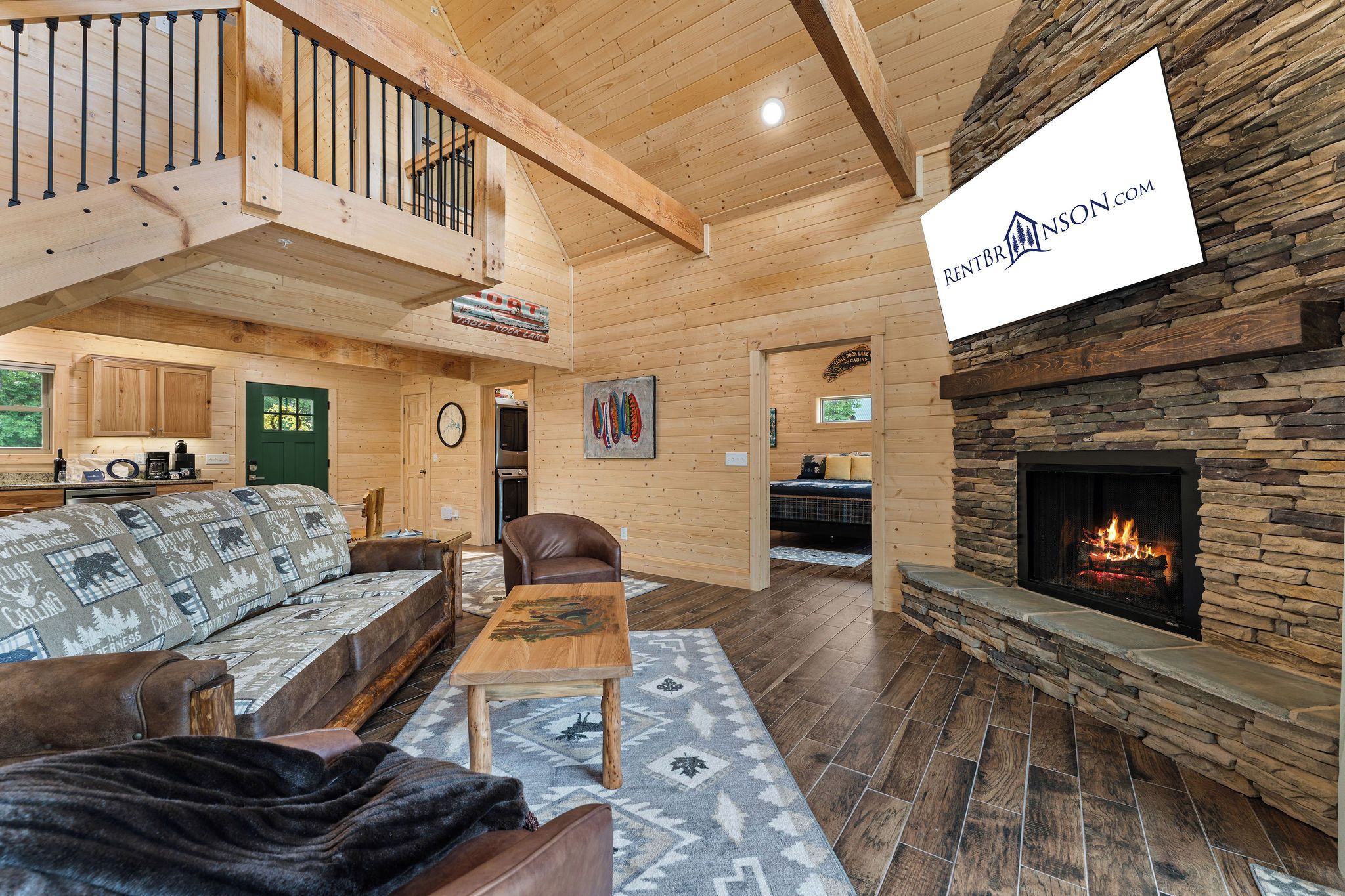 A cozy cabin interior with a wooden staircase, a fireplace, a sofa, a dining table, and a kitchen area.
