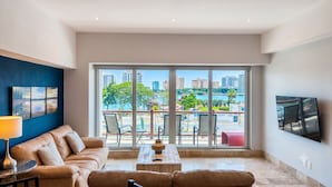 A modern living room with a sofa, a coffee table, and a TV mounted on the wall. - Deck12 2BR Premium Pool Access Parking (Puerto Vallarta)