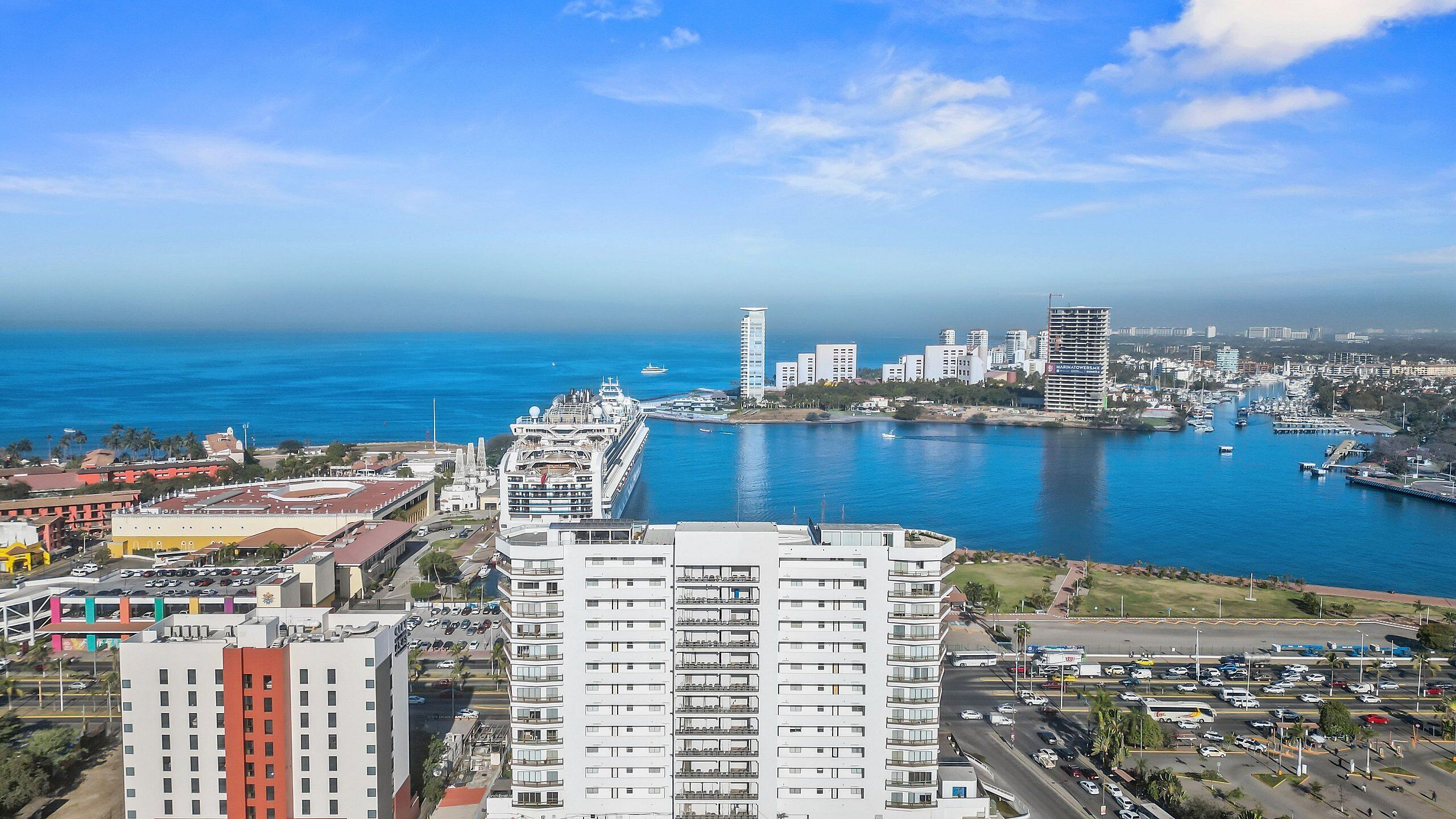 A coastal cityscape with a cruise ship docked, high-rise buildings, and a marina.