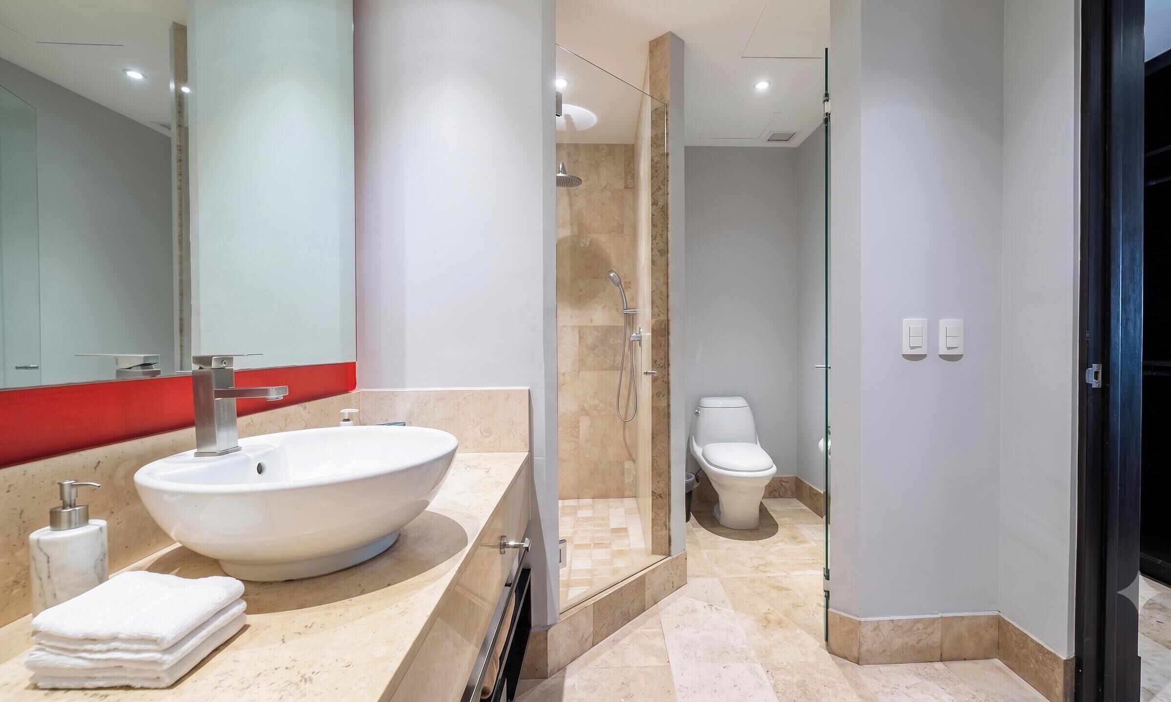A modern bathroom with a large sink, a glass-enclosed shower, and a toilet.