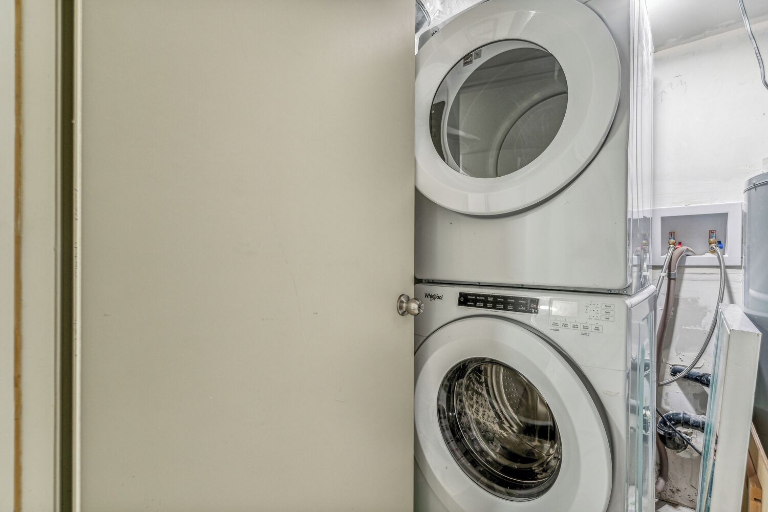 A stacked washer and dryer unit with a control panel and hoses visible.